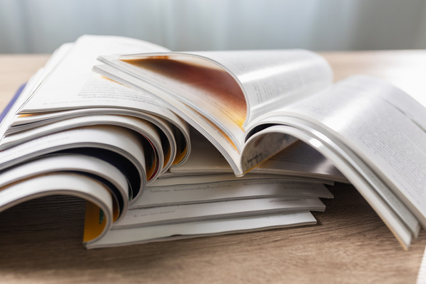 Stapel aufgeschlagener Zeitschriften auf einem Holztisch, die Seiten sind leicht gebogen und überlappen sich. - © onephoto - stock.adobe.com