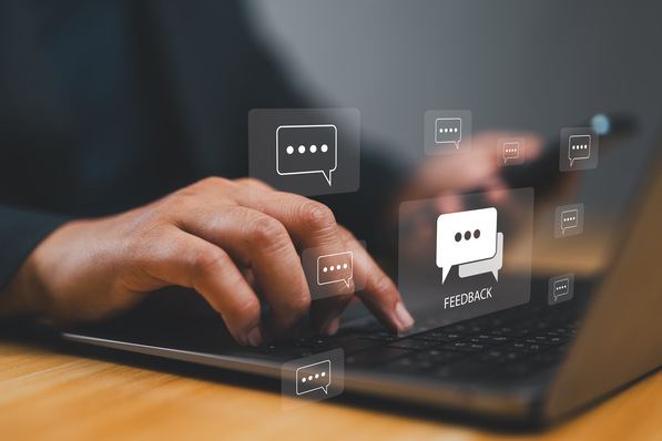 Hände tippen auf einem Laptop, in dem Sprechblasen mit der Aufschrift „Feedback“ schweben. - © Nirusmee - stock.adobe.com