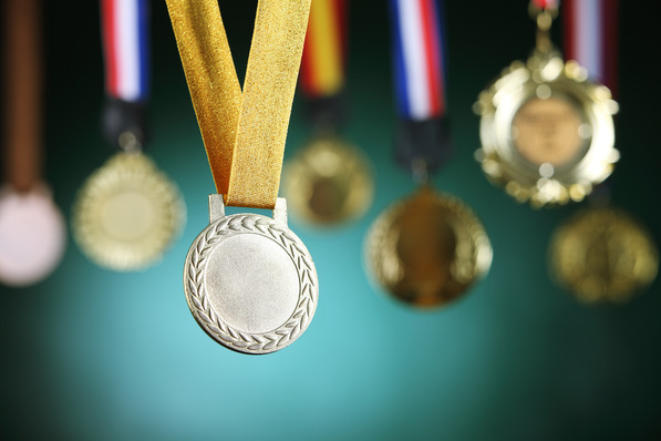 Nahaufnahme einer Silbermedaille mit einem gelben Band im Fokus, umgeben von unscharfen Medaillen im Hintergrund. - © eskay lim - stock.adobe.com