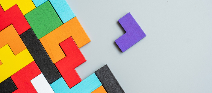 Bunte, Tetris-ähnliche Blöcke, die auf einer Oberfläche angeordnet sind, wobei sich ein einzelner violetter Block von einem grauen Hintergrund abhebt. - © Jo Panuwat D - stock.adobe.com