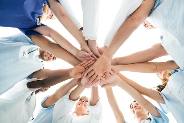 Mitarbeiter des Gesundheitswesens in OP-Kleidung und Laborkitteln bilden einen Kreis an den Händen und symbolisieren damit Teamwork und Einheit. - © Andrey Popov - stock.adobe.com
