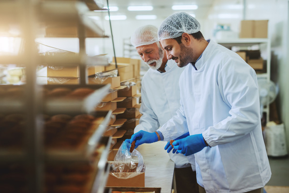 Zwei Bäcker in weißen Kitteln und Haarnetzen packen in einer Bäckerei Gebäck in Kartons. Sie lächeln und sind auf ihre Aufgabe konzentriert. - © Dusan Petkovic - stock.adobe.com