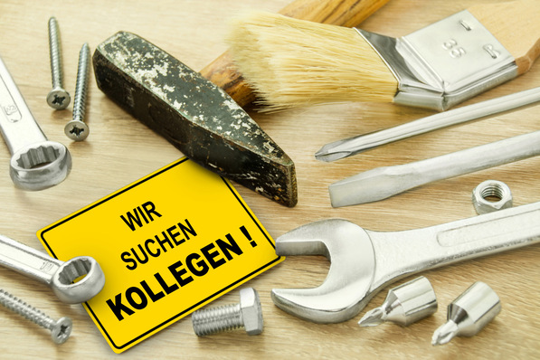 Werkzeuge und ein gelbes Schild mit dem deutschen Text „WIR SUCHEN KOLLEGEN!“ auf einer Holzoberfläche. - © PhotoSG - stock.adobe.com