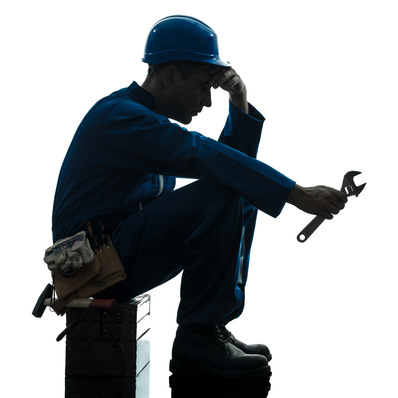 Silhouette eines Arbeiters in blauem Overall und Helm, der sitzt und einen Schraubenschlüssel hält, in der Nähe ein Werkzeuggürtel und eine Kiste. - © snaptitude - stock.adobe.com