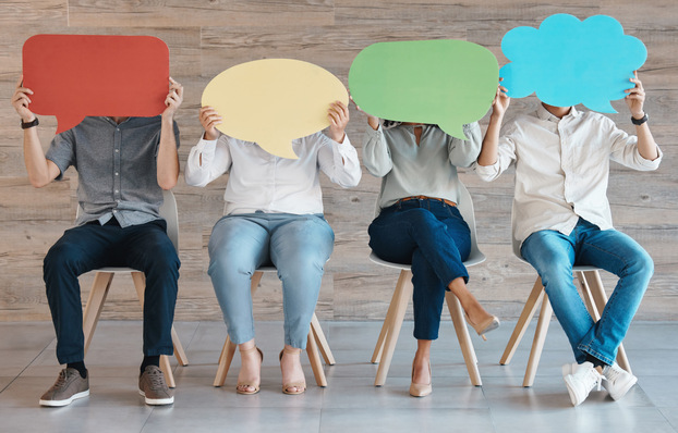 Vier Personen sitzen auf Stühlen und halten sich bunte Sprechblasenschilder vor das Gesicht. - © Charlize D/peopleimages.com - st