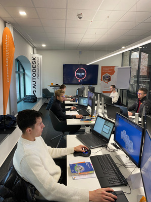 Mehrere junge Männer arbeiten an Computern mit CAD-Software in einem modernen Büro mit Bannern und einer Zeitschaltuhr an der Wand. - © Mensch und Maschine Deutschland GmbH